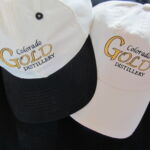Two hats with the colorado gold distillery logo on them.