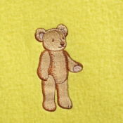 A teddy bear is embroidered on the yellow blanket.