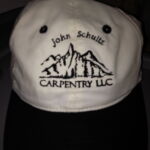 A white hat with black trim and the name john schultz carpentry llc