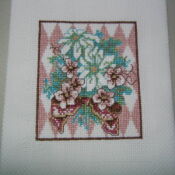 A cross stitch picture of flowers on a pink and white background.