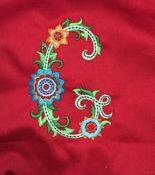 Ornate floral embroidered letter C on red fabric