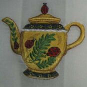 A yellow teapot with red and black flowers on it.